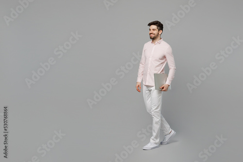 Full body young smiling cheerful happy fun cool caucasian IT man 20s he wearing basic shirt hold laptop pc computer isolated on plain grey color background studio portrait. People lifestyle concept.