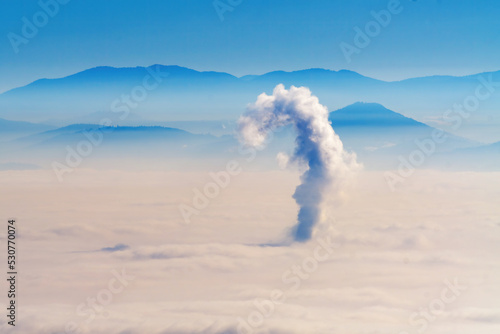 Foggy landscape with single plume of smoke from chimney above the city