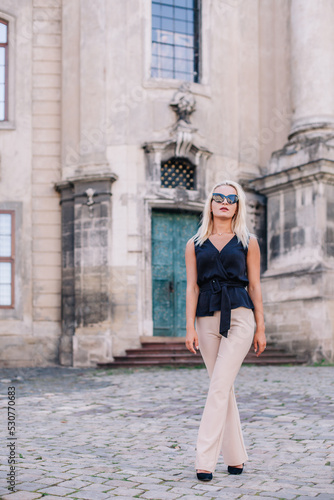 A young, slender blonde in beige pants and a black blouse walks the old streets of Lviv. Ukraine.