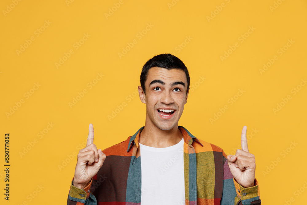 Young middle eastern man 20s wear casual shirt white t-shirt pointing index finger overhead indicate on workspace area copy space mock up isolated on plain yellow background People lifestyle concept.
