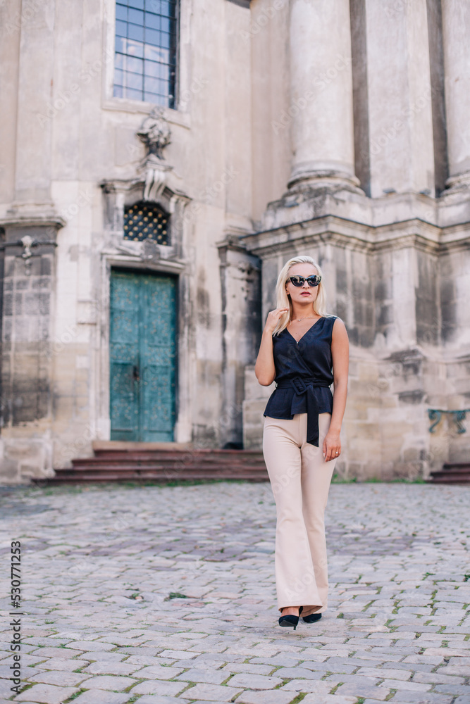 A young, slender blonde in beige pants and a black blouse walks the old streets of Lviv. Ukraine.