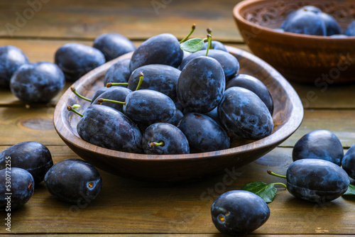 Ripe blue Fresh organic sweet plums just picked from the tree, walnut wood bowl plate indoors. Autumn Harvest of fruits rustic wooden dark black background leaf clay.
