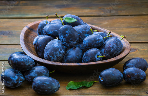 Ripe blue Fresh organic  sweet plums just picked from the tree, walnut wood bowl plate indoors. Autumn Harvest of fruits  rustic  wooden dark black background leaf clay.