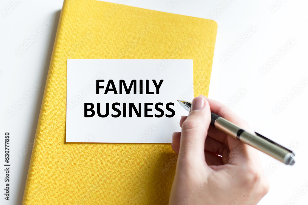Businesswoman writes in a notebook with a silver pen and hand hold card with text: FAMILY BUSINESS. Pink background. Business and education concept. Businesswoman writes in a notebook with a silver pen and hand hold card with text: FAMILY BUSINESS. Pink background. Business and education concept.