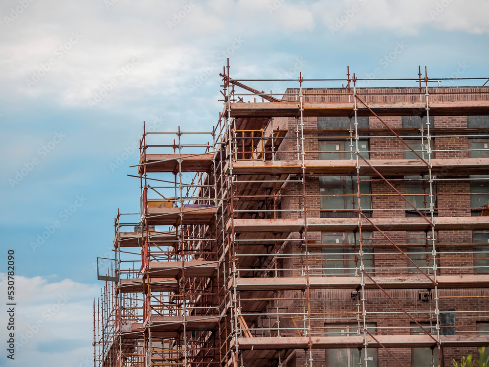 Scaffolding around new commercial office or residential building. Blue cloudy sky in the background. Property development. Scaffolding around new commercial office or residential building. Blue cloudy sky in the background. Property development.