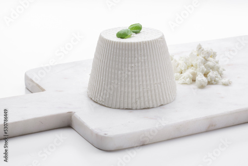 whole ricotta with basil leaf on a white marble cutting board