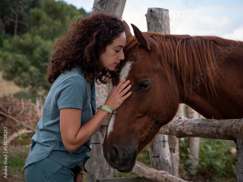 Brunette woman forming bond with an anglo- arab horse behind a wood fence in a field.