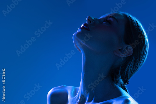Night life. Closeup portrait of young woman in neon light on dark blue background. Monochrome. Cyberpunk style, beauty, cosmetics concept.