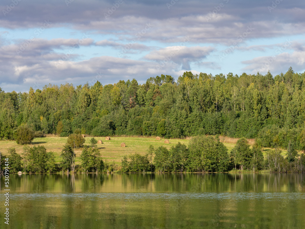 Autumn landscape in the Republic of Karelia, northwest Russia. Lake in calm weather, forest, haystacks on the field