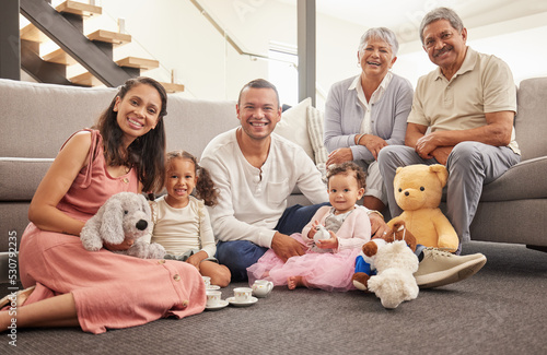 Portrait of a happy family having a tea party in a living room together, smiling and relaxing on a floor. Cheerful grandparents enjoying the weekend with their grandkid, being playful and having fun