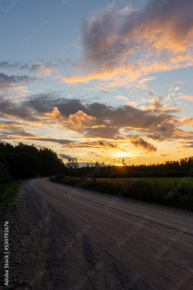 sunset on a rural dirt road with yellow and orange clouds