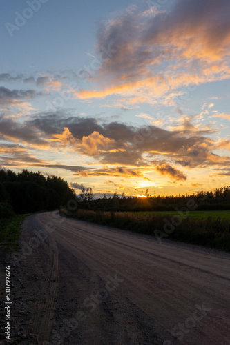 sunset on a rural dirt road with yellow and orange clouds