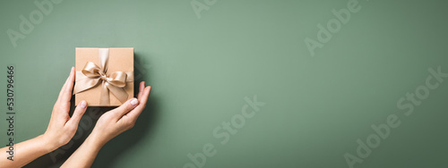 Obraz na plátně Female hands holding Christmas gift box on pastel green background