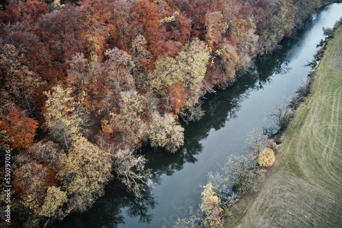 Aerial view of forest beside a river in beautiful autumn. Colorful Trees in yellow, red and green from above.