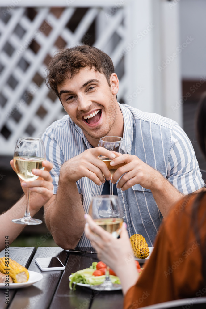 excited man holding glass with wine near friends during bbq party on backyard