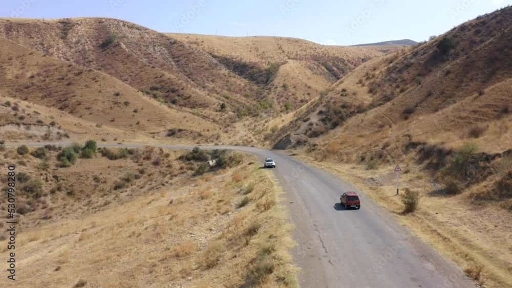 Traveling by car. A red car is moving along a mountain road in Kyrgyzstan. Peaceful natural background. Panorama of rocky mountains, hills and cliffs. Traveling by car. A red car is moving along a mountain road in Kyrgyzstan. Peaceful natural background. Panorama of rocky mountains, hills and cliffs.