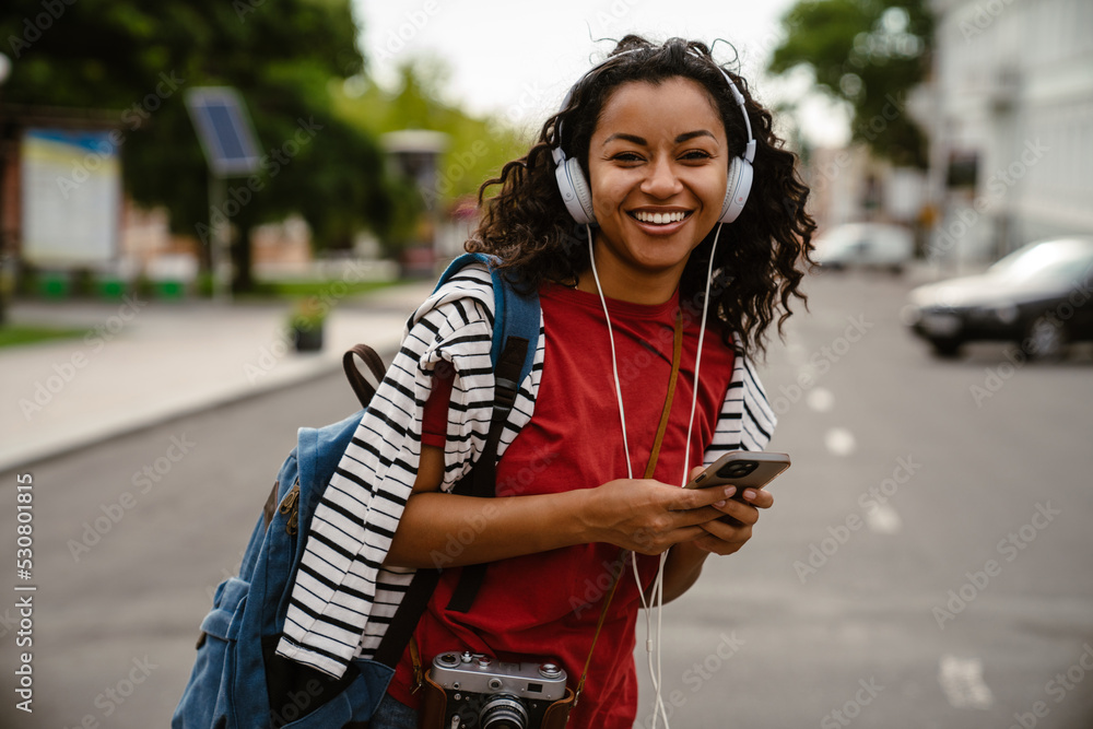 Young black woman in headphones using mobile phone outdoors