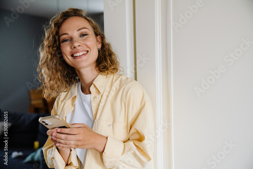 Tableau sur toile Young beatiful smiling curly woman with phone looking at camera