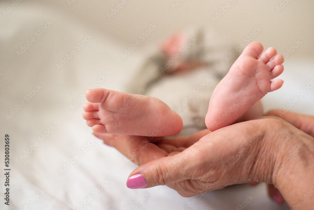 Woman's hand gently holds little feet newborn. Baby sleeping soundly and peacefully on white blanket. New worries and style life. Concept of child care, feeling safe, parent love. Woman's hand gently holds little feet newborn. Baby sleeping soundly and peacefully on white blanket. New worries and style life. Concept of child care, feeling safe, parent love.