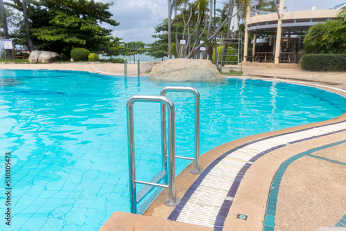 Ladder stainless handrails for descent into swimming pool. Swimming pool with handrail . Ladder of a swimming pool. Horizontal shot. stairs swimming pool. Stainless steel ladder