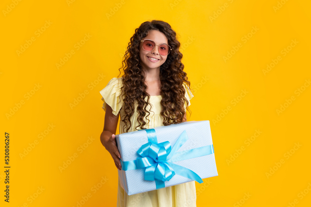 Happy teenage girl. Teenager child holding gift box on isolated yellow background. Gift for kids birthday. Christmas or New Year present box. Smiling kids emotions.