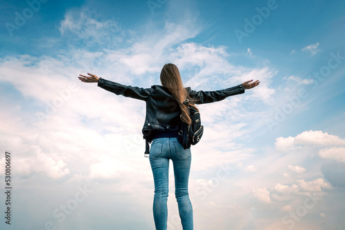 Young woman in a jacket stands with her hands raised up on a mountain in clouds. Concept of travel, freedom, enjoyment photo