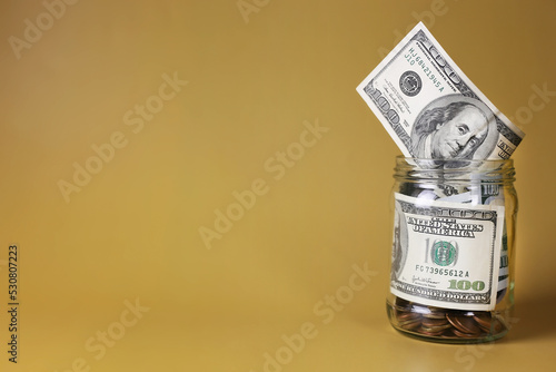 Dollars in a glass jar with coins on a yellow background. Money saving concept