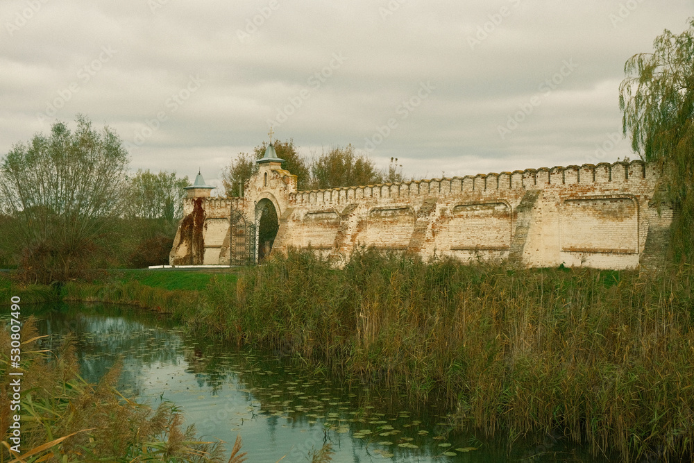 Ancient Cossack fortress. Brick walls, gates, a moat and a bridge leading to the fortress. Around the river with reeds, and brick walls for defending.