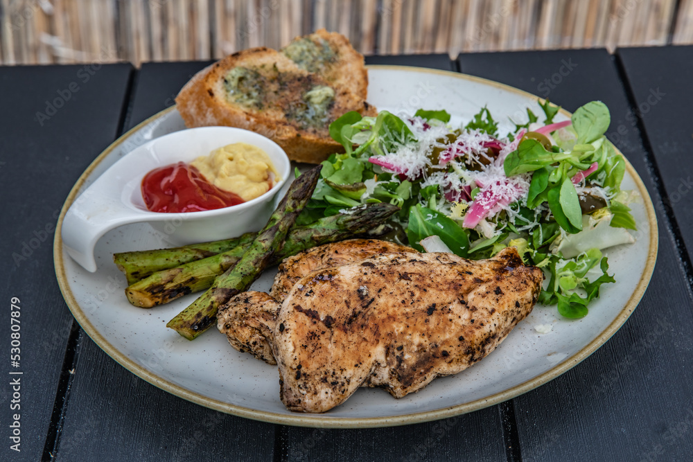Grilled chicken fillet with asparagus, mustard, ketchup, salad and toast