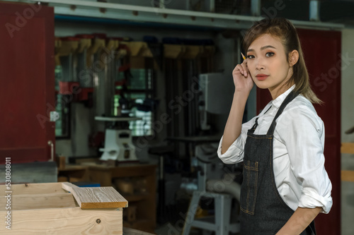 Young Asian female capenter in apron working in carpentry woodworking workshop, Carpenter woman concept photo