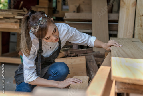 Young Asian carpenter woman working with wood project in carpentry workshop, Carpenter concept