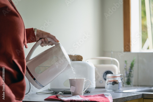 Pouring boiling water on a cup of tea with electric kettle in the morning. Unrecognizable person photo
