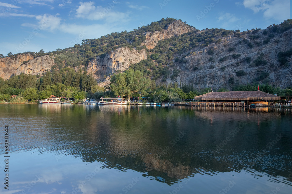 The rock-cut temple tombs of the ancient city of Kaunos in Dalyan, Muğla, Turkey. Beautiful view of Dalyan river with reed beds, excursion boats and carved tombs in the background.