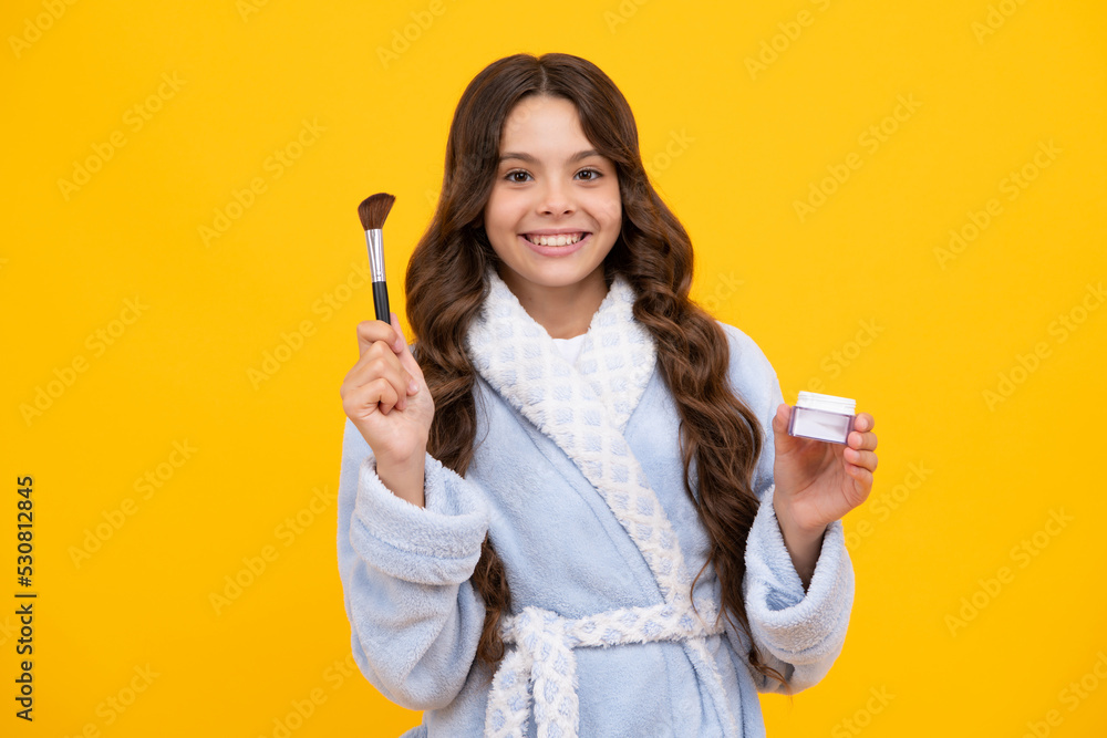 Beauty, make up and kids cosmetics. Teenage girl with brush applying blush to face isolated on yellow studio background. Beauty, make up and kids cosmetics. Teenage girl with brush applying blush to face isolated on yellow studio background.