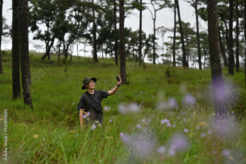 Asian adventurer man  using smartphone taking a photo at pine forest. © saltdium