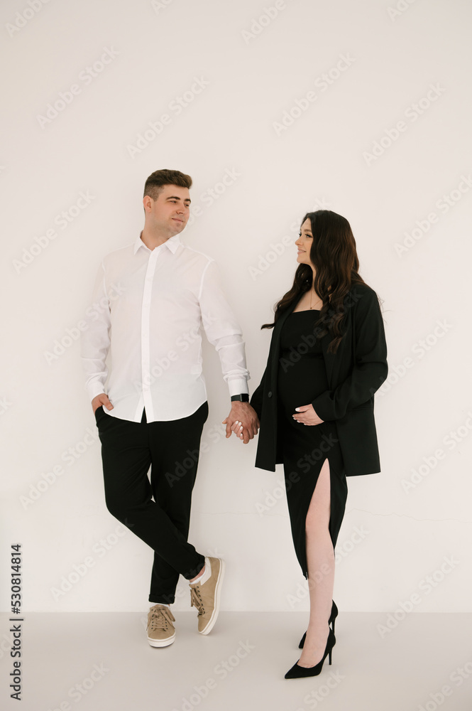 Young pregnant woman with her husband in stylish elegant black clothes on a light background Young pregnant woman with her husband in stylish elegant black clothes on a light background