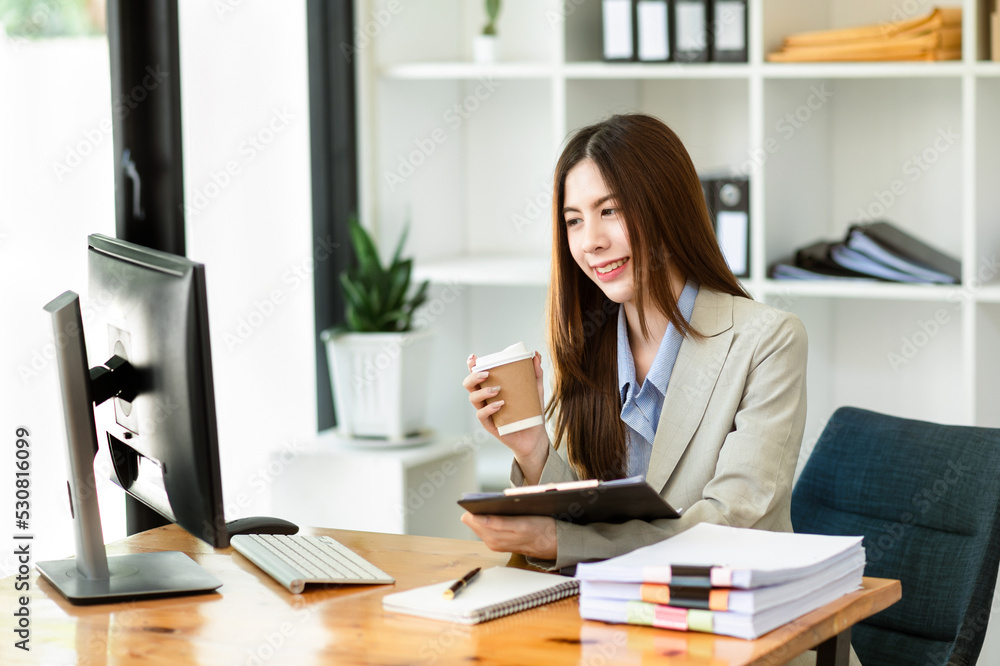 Confident beautiful Asian businesswoman typing laptop computer and digital tablet while holding coffee at office.. Confident beautiful Asian businesswoman typing laptop computer and digital tablet while holding coffee at office..