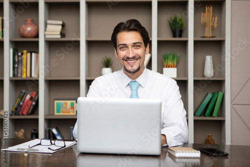 Young handsome smiling businessman working on laptop in the office