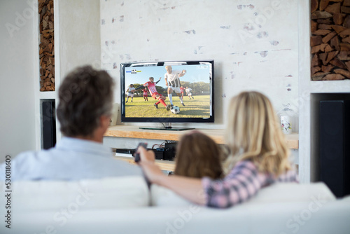 Caucasian family watching tv with football match on screen