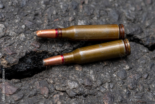 Cartridges with bullets with a displaced center of gravity lie against the background of cracked asphalt, selective focus. Concept: heavy damage, prohibited ammunition, war in Ukraine.