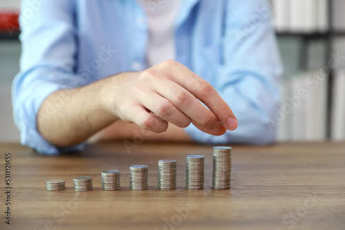 Business investment and saving growth for advertising concept. Businessman hand stacking coin growing on wood table and modern office background, meaning of tax or earning money