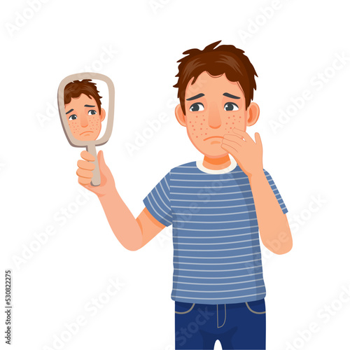 Anxious young man holding mirror looking at acne spot pimples on his face