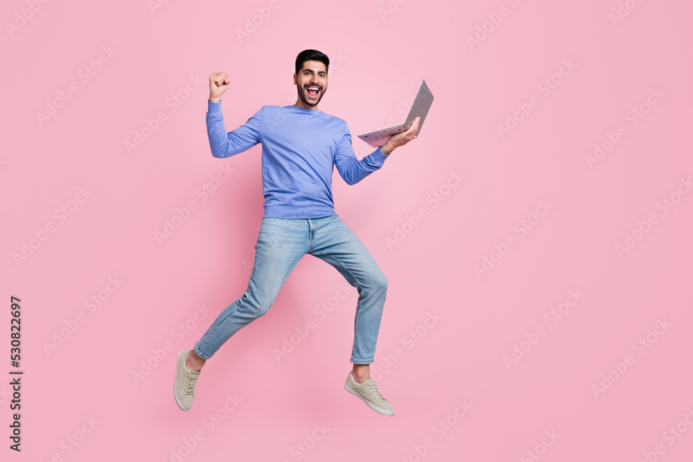 Full length photo of pretty lucky guy dressed blue pullover jumping high communicating modern device isolated pink color background