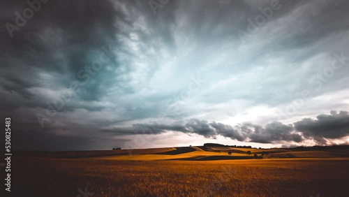 Time lapse of a sunset, dark clouds move away over the golden farmer's field in countryside