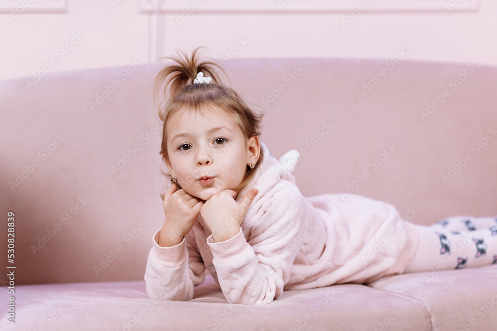 Little cute adorable Caucasian girl is lying alone on pink sofa and looking in camera in room. High quality photo Little cute adorable Caucasian girl is lying alone on pink sofa and looking in camera in room. High quality photo