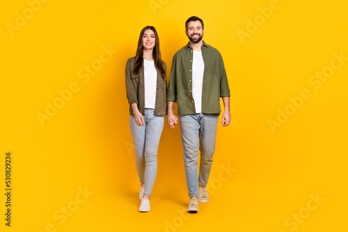 Full length body size view of attractive cheerful couple holding hands going isolated over bright yellow color background