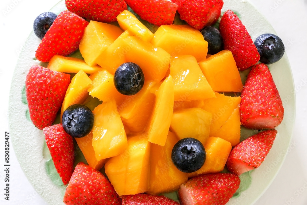 Obraz premium Top view close up of fresh fruits, strawberries, mango and blueberries topping a birthday cake