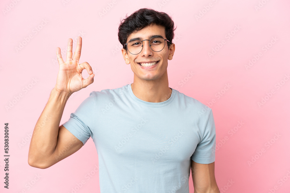 Young Argentinian man isolated on pink background With glasses and doing OK sign Young Argentinian man isolated on pink background With glasses and doing OK sign