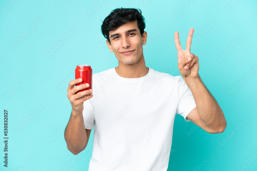Young Argentinian man holding a refreshment isolated on blue background smiling and showing victory sign