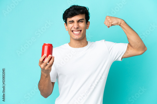 Young Argentinian man holding a refreshment isolated on blue background doing strong gesture